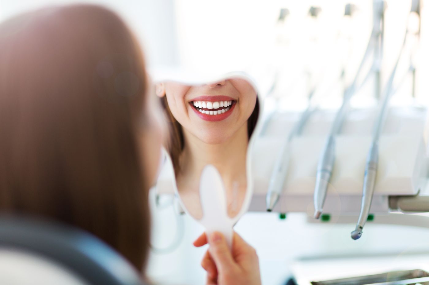 Woman holding mirror to show bright smile in dental office
