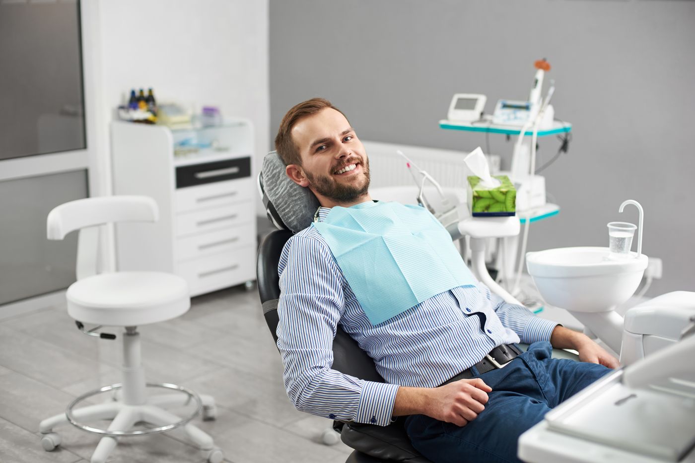 Man in dental chair with blue bib smiling during checkup