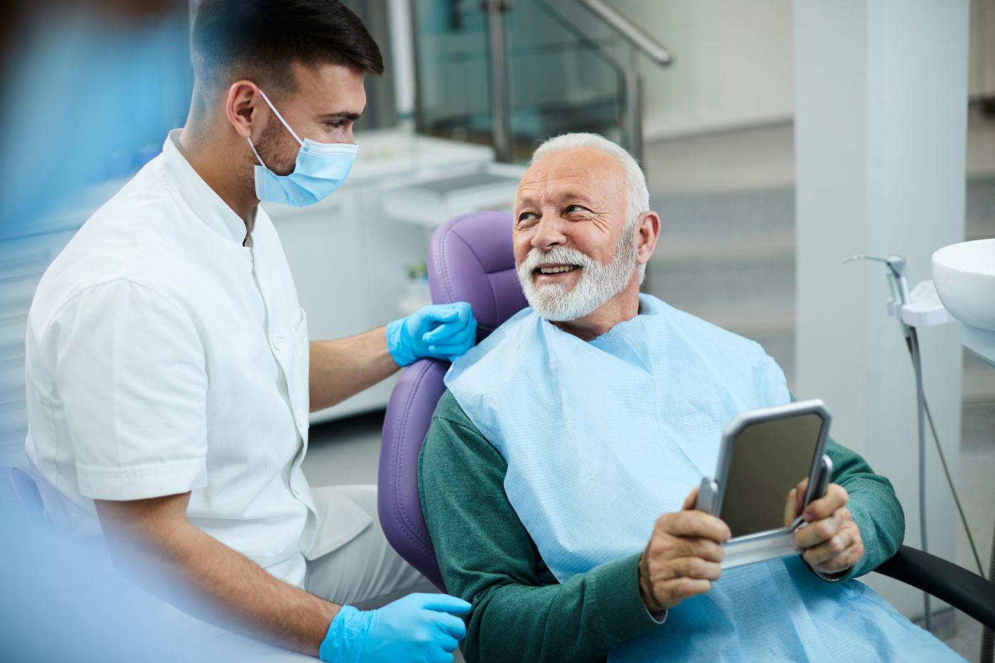 Dentist assisting elderly patient with handheld mirror during dental checkup