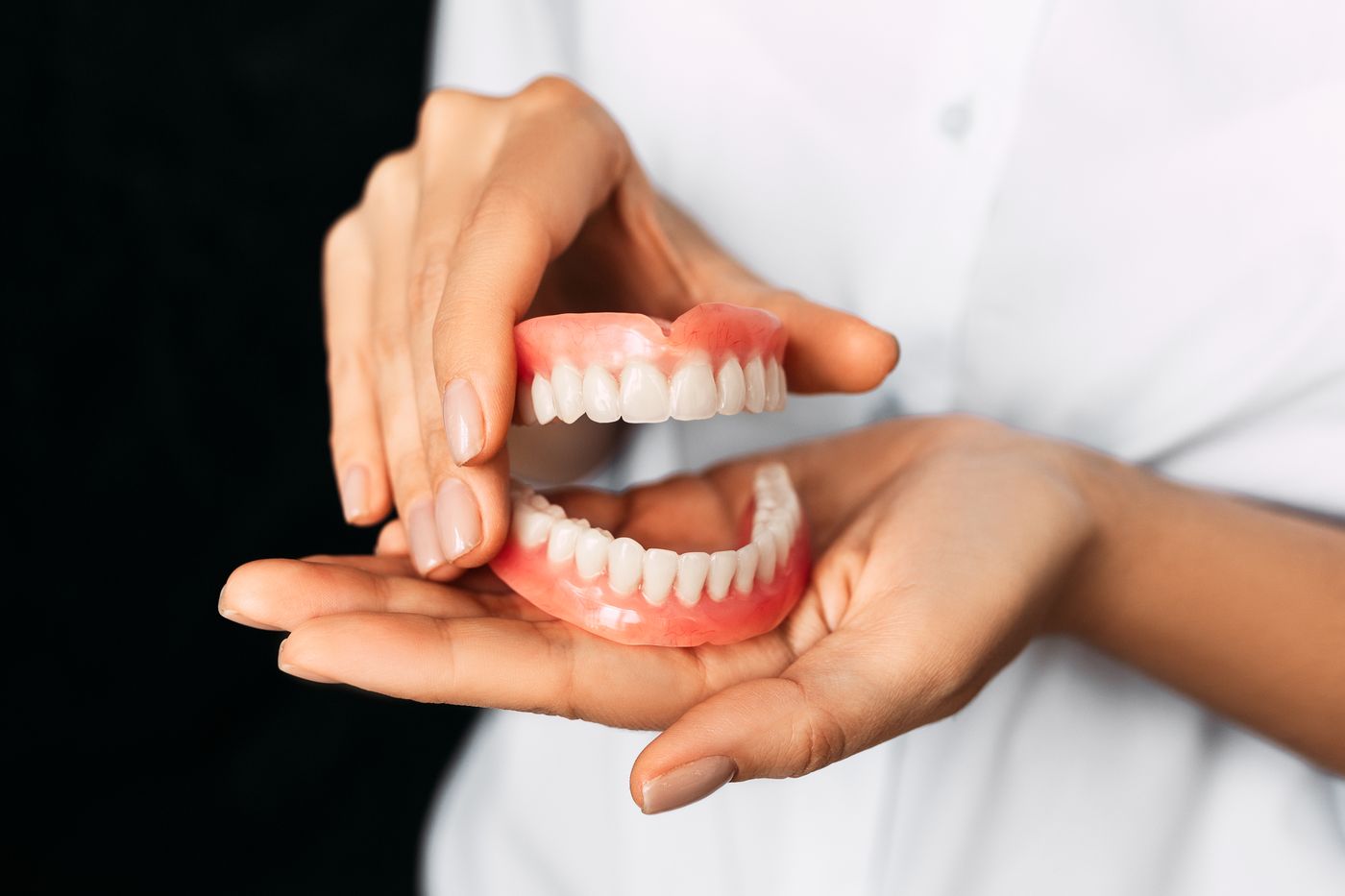 Dentist holding full dentures in hands against dark background