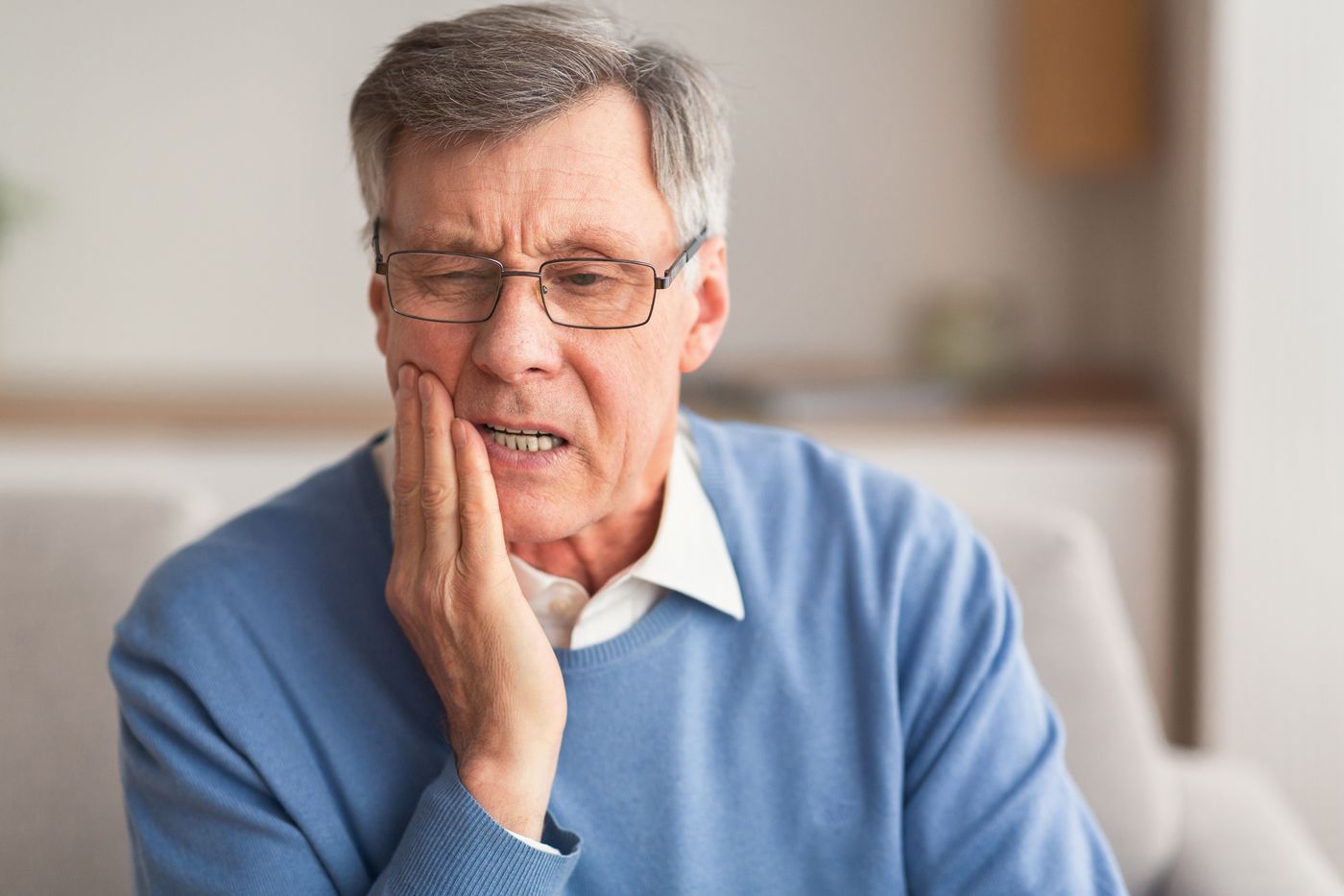 Senior man touching his cheek with a worried expression in a home setting